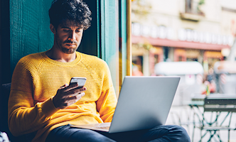 man-gele-trui-telefoon-en-laptop