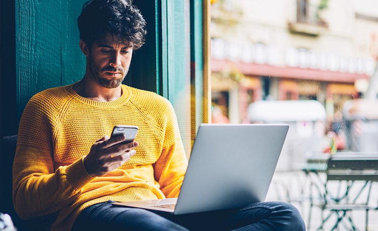 man in gele trui met telefoon en laptop